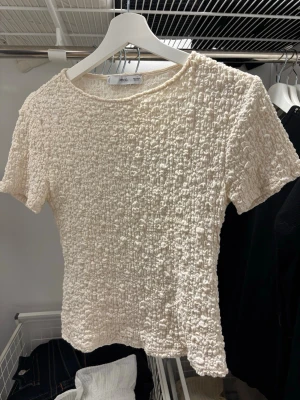 Vit ribbad topp med kort ärm - Säljer en söt vit topp med ribbad struktur och korta ärmar. Toppen är figurnära och har en lätt croppad passform som passar perfekt till jeans eller kjol. Enkel och stilren design utan synliga märken eller loggor. Har använts få gånger så som ny❣️