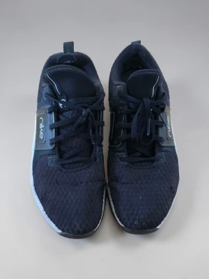 Svarta Nike sneakers med mesh 42 - Säljer ett par svarta Nike sneakers med ovandel i meshmaterial och klassisk snörning. Skorna har en låg silhuett och detaljer i plast vid snörningen. Sulan är vit med svarta inslag och loggan syns tydligt på sidan. Perfekta för en sportig och avslappnad stil.