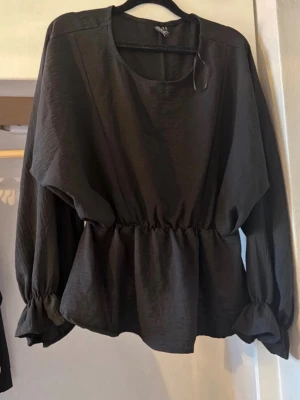 Svart blus med resår i midjan - Säljer en svart blus från Vila med rund halsringning, resår i midjan och vida ärmar med resår vid ärmsluten. Blusen har en avslappnad passform och är gjord i ett lätt, mjukt tyg som ger ett snyggt fall. Perfekt att styla med både jeans och kjol.