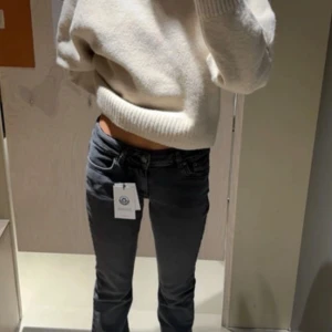 Lowwaist utsvängda gråa jeans - Säljer ett par mörkgrå utsvängda med klassisk femficksdesign och bälteshällor. Jeansen har en tight passform och är tillverkade i stretchigt denimtyg för extra komfort. Perfekta för en trendig och avslappnad look. Färgen är mörkgrå och passar till det mesta!