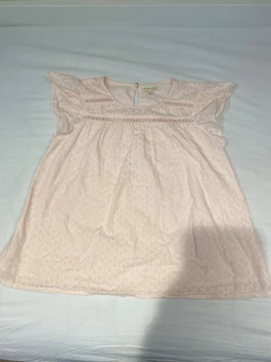 Ljusrosa blus med spetsdetaljer❣️ - Söt ljusrosa blus från Pompdelux med korta ärmar och fina spetsdetaljer upptill. Blusen har ett diskret mönster i tyget och en knapp i nacken. Super söt till sommaren.💞                                                                               Säljer pga att jag inte använder längre💌