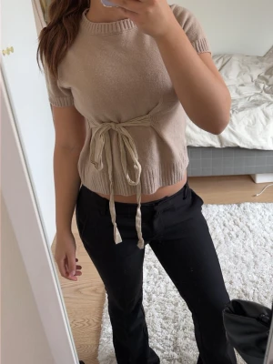 Beige stickad topp från Zara - Säljer en beige stickad topp från Zara med korta ärmar och rund hals. Toppen har en snygg knyt-detalj i midjan som ger en trendig look. Använd 1 gång så är som ny💕