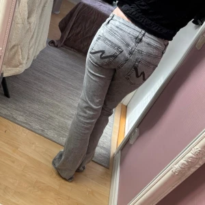 Gråa bootcut jeans från Wrangler - Säljer ett par gråa bootcut jeans från Nelly. Jeansen har fem fickor och en snygg tvättad look. Perfekta för dig som gillar retrostil och vill ha ett par jeans som sticker ut.