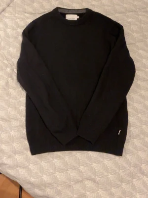 Svart stickad tröja Casual Friday - En stilren svart stickad tröja från Casual Friday. Tröjan har rund halsringning, långa ärmar och ribbade muddar vid ärmslut och nederkant. Perfekt basplagg för garderoben och enkel att matcha med olika outfits.