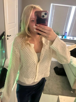 Vit virkad kofta med knappar - Snygg vit kofta med virkat mönster och knäppning framtill. Koftan har långa ärmar och ribbade muddar vid ärmslut och nederkant. Perfekt att slänga över ett linne för en chill look.