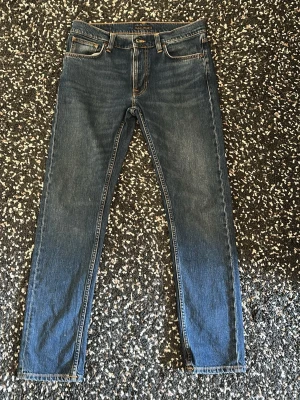 Blå Nudie Jeans  - Säljer ett par klassiska blå jeans från Nudie Jeans med raka ben och fem fickor. Jeansen har snygga kontrastsömmar och är gjorda i slitstark denim. Modell lean Dean i färgen Troubled sea. 