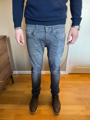 Dondup george jeans - Säljer ett par grå slim fit jeans från dondup med snygg tvättad look och klassiska fem fickor. Jeansen har låg midja, smal passform och diskreta detaljer vid fickorna. Perfekta för en trendig och avslappnad stil. 