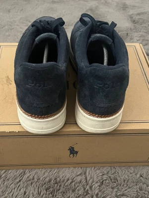 Mörkblå Polo Ralph Lauren sneakers - Snygga mörkblå sneakers från Polo Ralph Lauren i mocka med klassisk låg profil och vita sulor. Diskret Polo-logga bak på hälen och på yttersulan. Perfekta för dig som gillar stilrena och tidlösa skor med en sportig touch. Om du tycker det är för dyrt kan vi diskutera om bättre pris. 