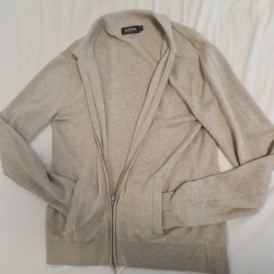 Beige kofta med dragkedja  - Snygg beige kofta  med dragkedja framtill. Perfekt för lager-på-lager och har en klassisk krage. Långärmad design med ribbade muddar och nederkant för en stilren look.