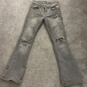 Grå bootcut jeans med slitningar - Säljer ett par gråa bootcut jeans med hål vid knäna och låret som jag klippt själv. Jeansen har låg midja. 