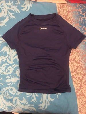 Mörkblå träningströja från DFYNE - Kortärmad mörkblå träningströja från DFYNE med logga på bröstet och nacken. Tillverkad i ett stretchigt funktionsmaterial som passar perfekt för gym eller löpning. Tight passform och rund halsringning.