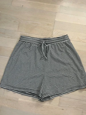 Randiga shorts från SKØN Copenhagen - Säljer ett par svartvita randiga shorts från SKØN Copenhagen. De har snörning i midjan och är tillverkade i mjukt bomullsmaterial. Perfekta för varma dagar och har en avslappnad passform.