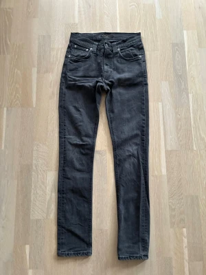 Svarta skinny jeans från Nudie Jeans - Snygga svarta skinny jeans från Nudie Jeans med klassisk femficksmodell och dragkedjegylf. Jeansen har en smal passform och är tillverkade i mjuk denim som sitter bekvämt. Perfekta för en stilren och avslappnad look. Storlek 28x32