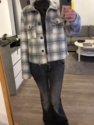 Rutig jacka från ONLY - Snygg rutig jacka från ONLY i blått, vitt och grått. Jackan har klassisk krage, knäppning framtill och två bröstfickor med lock. Perfekt för dig som gillar en trendig och avslappnad stil.