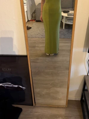 Lång grön klänning med tight passform - En stilren långklänning i ljusgrön nyans med tight passform. Klänningen är ärmlös och har en enkel, rak design som framhäver siluetten. Perfekt för dig som gillar minimalistiska och moderna plagg.