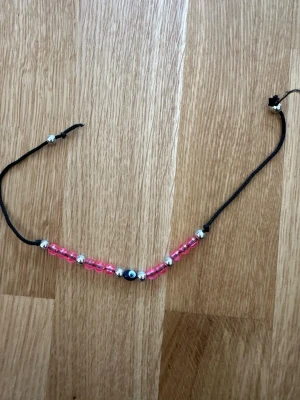 Svart armband med rosa pärlor - Snyggt armband med svart justerbart band och pärlor i rosa och silver. Detta armbandet har inte använts många gånger men det finns däremot tecken på mindre slitage.