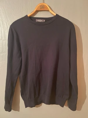 Svart tröja från Dressman - En stilren svart tröja från Dressman med rund halsringning och långa ärmar. Tröjan har en enkel design utan tryck eller mönster och ribbade muddar vid ärmslut och nederkant. Perfekt basplagg till garderoben. Storlek M men passar S