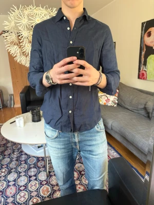 Mörkblå linneskjorta  - Säljer en mörkblå skjorta i linne med klassisk krage och vita knappar. Perfekt för sommarn 