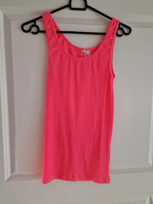 Rosa ribbad tanktop från H&M - Säljer en snygg och enkel rosa tanktop från H&M. Toppen är ribbad och har breda axelband samt rundad halsringning. Perfekt att matcha med jeans eller shorts för en avslappnad look. Materialet är mjukt och stretchigt för extra komfort.