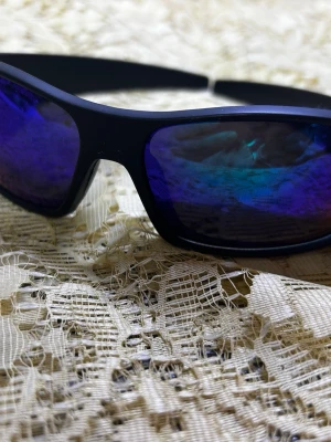 Svarta sportiga solglasögon - Säljer ett par svarta solglasögon med spegelblå linser och sportig, böjd form. Bågarna är i plast och designen är clean och modern, perfekt för dig som gillar en aktiv stil. Sitter skönt och ger cool vibe till din look.