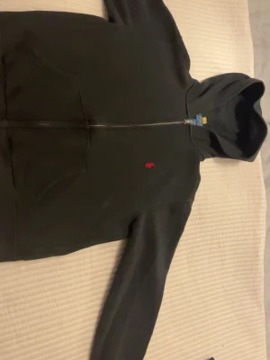  Svart hoodie från Polo Ralph Lauren - OANVÄND. ÄKTA. PRIS KAN DISKUTERAS. Klassisk svart hoodie med dragkedja från Polo Ralph Lauren. Har huva, kängurufickor och den ikoniska röda logotypen broderad på bröstet. Perfekt för en avslappnad och stilren look. Tillverkad i mjukt bomullsmaterial.