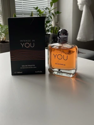 Intense In You Eau de Parfum 100ml - Intense In You Eau de Parfum från Fanocity i en elegant, fyrkantig glasflaska med rund silverfärgad kork. Doften har en varm, bärnstensfärgad vätska och kommer i en stilren svart kartong med kopparfärgade detaljer. Flaskan rymmer 100 ml.