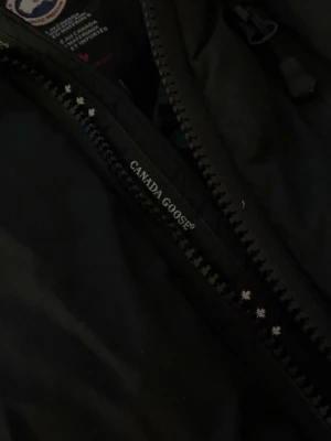 Svart dunjacka från Canada Goose - Säljer en svart dunjacka från Canada Goose med dragkedja och klassisk logga på insidan. Jackan är tillverkad i slitstarkt material och fylld med dun för maximal värme. Perfekt för kalla vinterdagar och har en stilren look. Kvitto finns med!!