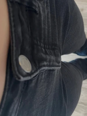 Svarta bootcut jeans med mid midja - Säljer ett par svarta bootcut jeans med mid midja och klassisk femficksdesign. Jeansen har en silvrig knapp framtill och smal passform som sitter tight hela vägen ner. Perfekta till en avslappnad eller trendig look.