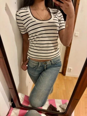 Randig ribbad topp i vitt och svart - Kortärmad topp med svart-vita ränder och ribbad struktur. Modellen har en rund ringning och kan bäras både normalt och offshoulder. Tunn och stretchig, perfekt till jeans eller kjol. Enkel och stilren design utan synligt märke. Köpt för 600kr