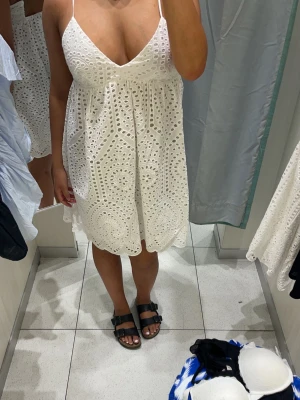 Vit somrig klänning med broderi - Superfin vit kortklänning med broderade detaljer och tunna axelband. Klänningen har v-ringning, knyt i ryggen och är ärmlös. 