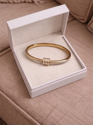 18K guld pläterade armband  - Snyggt armband i guldfärgad metall med tre ringar i mitten, dekorerade med små vita pärlor. Armbandet har en stilren och modern design med gnistrande detaljer längs sidorna. Perfekt accessoar för att lyfta din outfit.