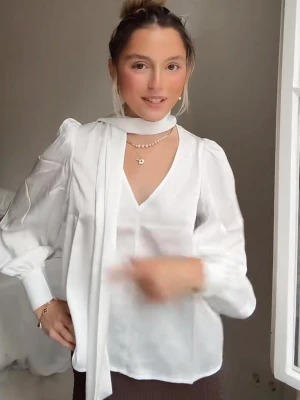 söker!!!!!!!!rVit blus med scarf-detalj - Stilren vit blus med v-ringning och långärmade puffärmar. Blusen har en elegant scarf-detalj runt halsen som kan knytas eller hänga löst. Materialet ser ut att vara lätt och något transparent, vilket ger en luftig känsla. Perfekt för att skapa en chic look.