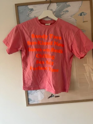 Rosa t-shirt med neontext - Cool rosa t-shirt med orange neontext framtill som ger sommarkänsla. Den är stor i storleken har den själv som 155cm