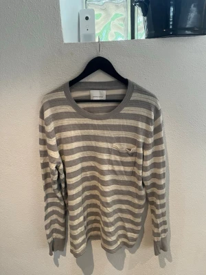 Randig långärmad tröja grå/vit - Säljer en randig långärmad tröja i bomull från Samsøe & Samsøe. Stilren modell i grå och beige toner med bröstficka. Använd men fortfarande i fint skick. Väldigt mjuk och skön och passar både till vardags och lite mer uppklätt. Storlek: L Märke: Samsøe & Samsøe Färg: Grå / beige randig Skriv gärna om du har frågor!