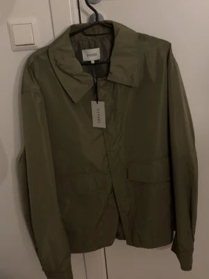 Overshirt  - Snygg olivgrön vindjacka från Sandö med klassisk krage och dold dragkedja framtill. Jackan har två stora fickor och är tillverkad i ett lätt, vindtätt material som passar perfekt för blåsiga dagar. Enkel och stilren design som funkar till det mesta aldrig använt perfekt till våren köpt för 900 .