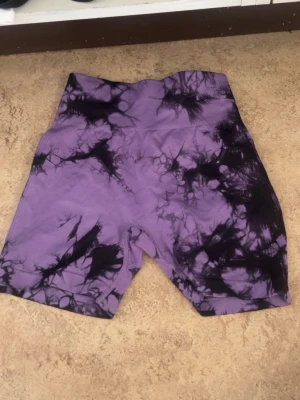 Lila och svarta seamless träningsshorts - Säljer ett par lila seamless träningsshorts med svart tie-dye mönster. Shortsen är tillverkade i 90% nylon och 10% elastan vilket ger en stretchig och bekväm passform. Perfekta för gymmet eller löpning.