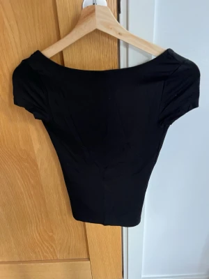 Svart top med djup rygg, från Gina Tricot - Snygg svart top med korta ärmar och en djup, rundad rygg. Tight passform och stretchigt material som sitter skönt mot kroppen. Perfekt att styla till olika outfits för en trendig look.