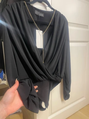Svart omlott body från Zara - Snygg svart body från Zara med omlott skärning framtill och djup v-ringning. Långa ärmar och mjukt, stretchigt material som sitter bekvämt. Perfekt att styla med kedjesmycke för en trendig look. Klassisk och enkel design som passar till mycket.