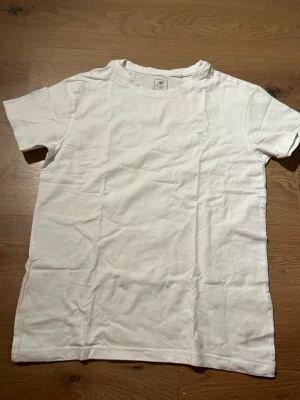 Vit t-shirt från 4F i bomull - Klassisk vit t-shirt från 4F med rund hals och diskret logga broderad på bröstet. Tillverkad i mjuk bomull som känns skön mot huden. Perfekt basplagg för alla tillfällen och enkel att matcha med andra plagg.