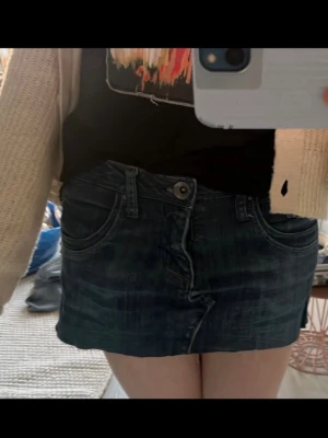 Mörkblå jeanskjol  - Kort mörkblå jeanskjol med rå kant nertill. Kjolen har dragkedja och knapp framtill samt en extra liten ficka med dragkedja, coola fickor. 