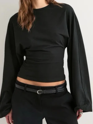 Nelly figursydd tröja  - Stilren svart croppad topp med långa, vida ärmar och rund halsringning. Toppen har en tight passform i midjan och är perfekt för en trendig och enkel look. Tillverkad i mjuk bomull som känns skön mot huden. (Med prislapp)