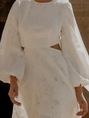 Student klänning - Superfin vit kort klänning med puffiga långärmar och diskreta cut-outs i midjan. Klänningen har en rund halsringning och är tillverkad i ett lätt, blommigt mönstrat tyg som ger en elegant känsla.