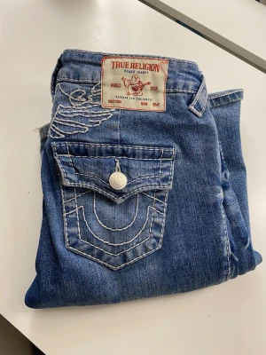 True Religion jeans med brodyr - Säljer mina True Religion‑jeans i blått! Hästsko‑broderi på bakfickorna – klassiskt True Religion‑utseende. Stl W25 Jeansen är i bra skick men lite nertrampade där nere o stora för mig därför säljs dem. Jag vill gärna köpa nya eller byta med någon som har liknande💞 så pris/bud kan ni skriva till mig💞 