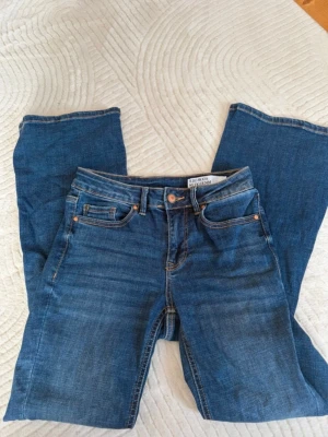 Blå bootcut jeans från B.Young - Säljer ett par klassiska blå bootcut jeans från B.Young. Jeansen har fem fickor, normalhög midja och snygga kontrastsömmar. Tillverkade i mjukt denimtyg som sitter skönt och ger en avslappnad look. Stolek xs/30, använd 1 gång