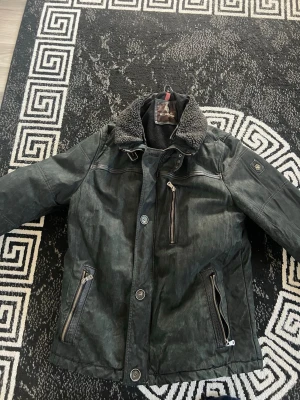 Svart jacka med fårskinnskrage - Cool svart jacka från Gulliver med fårskinnskrage och flera dragkedjor. Jackan har en quiltad känsla, bröstficka med dragkedja och två snedställda fickor framtill. Insidan är randig och mjuk, perfekt för kalla dagar.