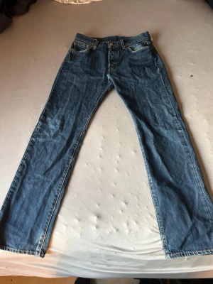 Levi’s 501 blåa - Klassiska blå jeans från Levi's med rak passform och fem fickor. Jeansen har en snygg tvättad look och är tillverkade i slitstarkt denim. Perfekta för dig som gillar tidlös stil och vill ha ett par jeans som funkar till allt.