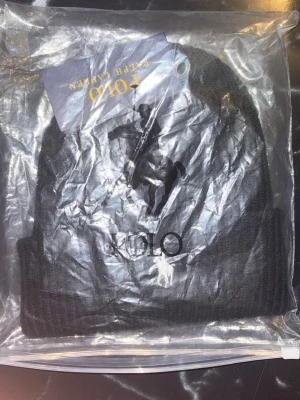 Svart ribbstickad mössa Polo Ralph Lauren - Säljer en svart ribbstickad mössa från Polo Ralph Lauren med den klassiska vita broderade polospelaren framtill. Mössan har uppvikt kant och är tillverkad i mjukt material som håller dig varm och stilren under kalla dagar.