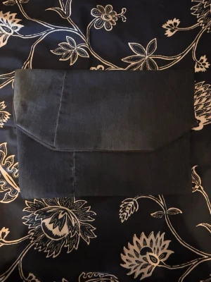 Mörkblå jeansdatorväska med ljusblå ficka - Unik datorväska i mörkblått jeanstyg med vikbart lock. Baksidan har en ljusare jeansficka med handritad blomma, perfekt för småprylar. Väskan har en enkel, stilren design och passar dig som gillar denim och personliga detaljer. Gjort för hand så inte perfekt, men ett perfekt val för miljön!🌏 Passar 13-14 tums eller mindre datorer.🤗Materialet inuti är vattentätt🌊