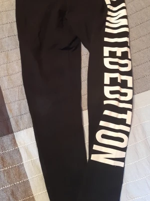Svarta training leggings med vit text från Golddigga  - Säljer ett par svarta leggings med stor vit text längs ena benet där det står 'LIMITED EDITION'. Tight passform och stretchigt material som sitter snyggt. Perfekta till en avslappnad och trendig look. Jag tror är det större än storlek 42, mått på bilderna. 