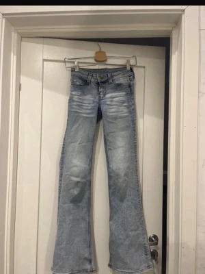 Ljusblå bootcut jeans från Cheap Monday - Säljer ett par ljusblå bootcut jeans från Cheap Monday med slitna detaljer och klassisk femficksmodell. Jeansen har en snygg tvätt och vida ben som ger en retrovibe. Perfekta för dig som gillar en avslappnad men trendig stil.